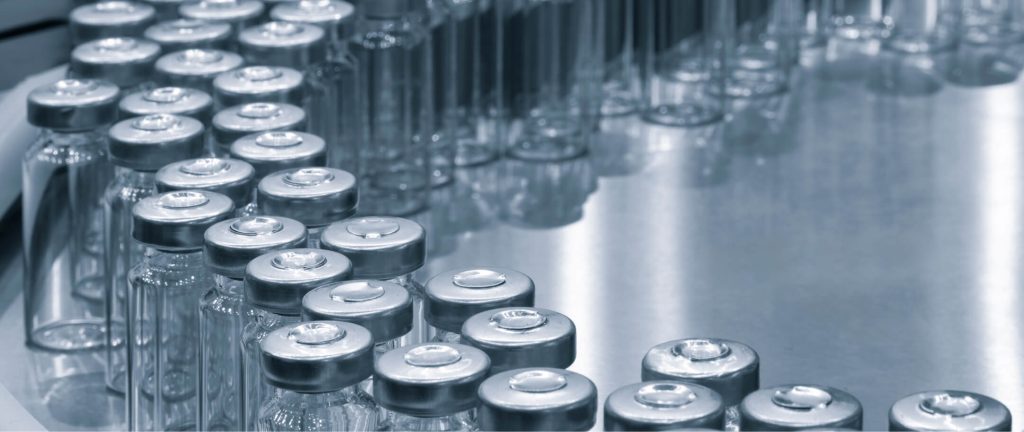 Sterile glass vials with aluminium caps on a stainless steel conveyor, used in pharmaceutical manufacturing or medical equipment packaging.